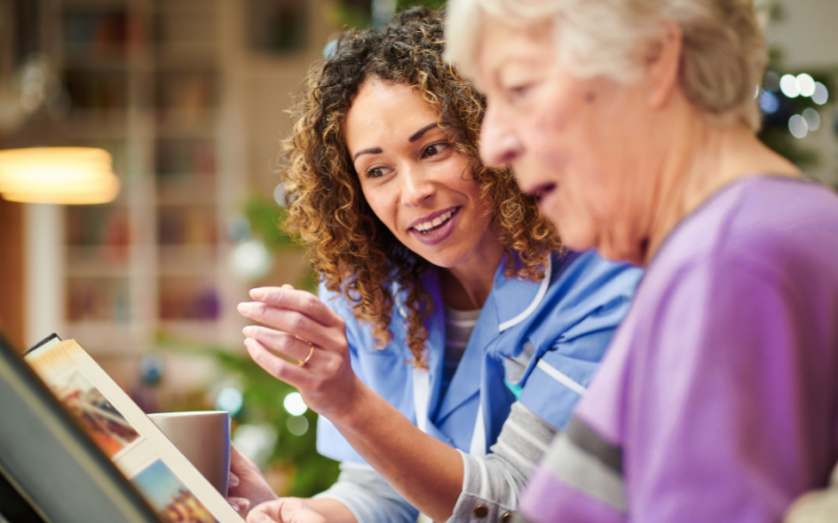 Elderly woman suffering with dementia looking through a memory book with her care worker in a home setting.