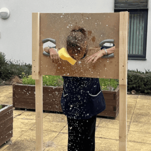 A carer in uniform being hit with a wet sponge at a family fun day event.
