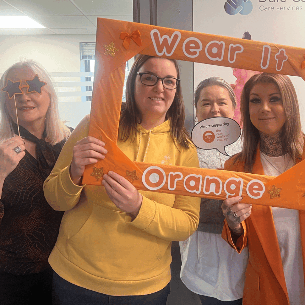 Group of four dressed in orange holding a sign that says 'Wear It Orange' and 'We are supporting the Care Workers' Charity'.
