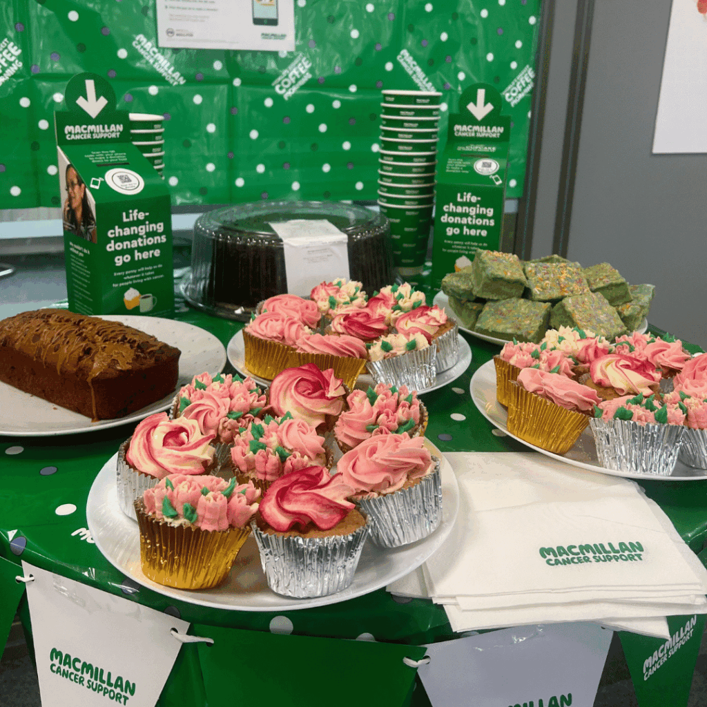 A variety of cakes and other baked goods with a green background and 'Macmillan Cancer Support' bunting on the table.