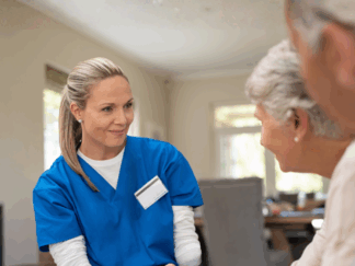 Carer sat in a living room setting, opposite are two elderly service users speaking to her as she respectfully listens.