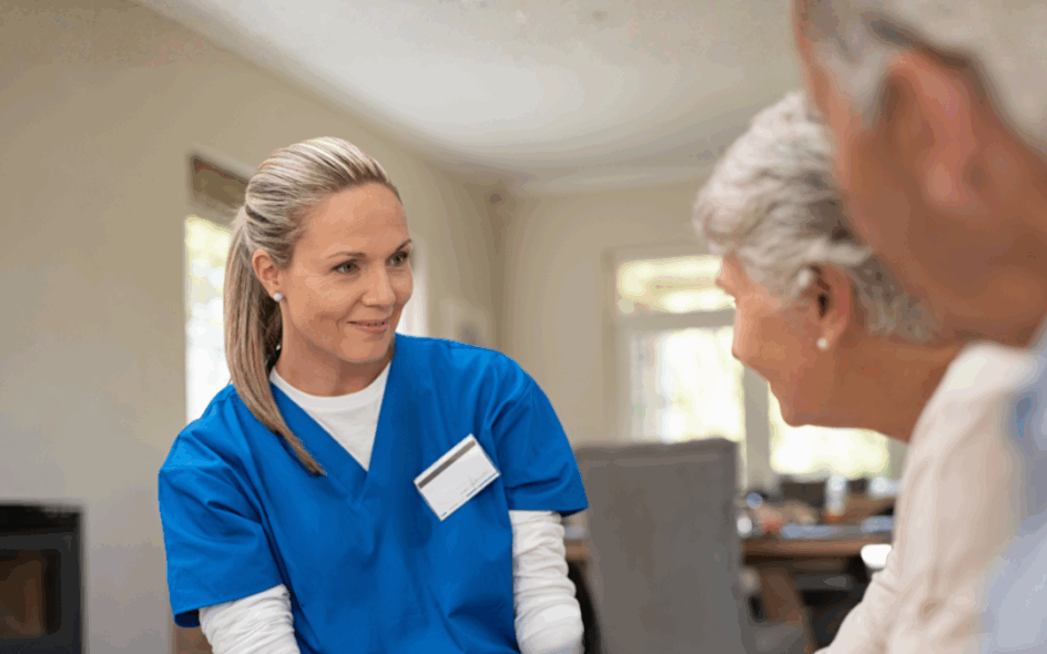Carer sat in a living room setting, opposite are two elderly service users speaking to her as she respectfully listens.