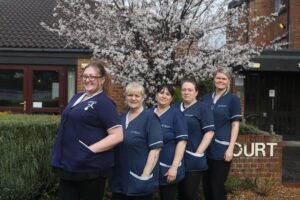 Pictured is five of Dale Care's caring care workers outside, stood together and smiling towards the camera in their navy uniforms.
