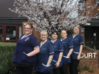 Pictured is five of Dale Care's caring care workers outside, stood together and smiling towards the camera in their navy uniforms.